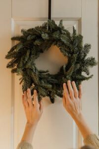 Hands placing a festive holiday wreath on an indoor door.