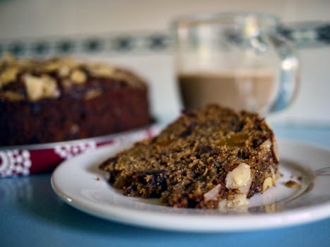 Close-up of a nutty fruit cake slice on a plate with a cup of coffee in the background. Perfect for dessert lovers. 